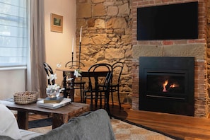 A cozy living room with a stone wall, a fireplace, a dining table with chairs, and a comfortable sofa.