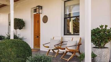 A porch with two rocking chairs, a wooden door, and a window with a view of trees.