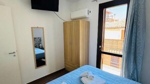A room with a bed, a wardrobe, a mirror, and a window with a view of buildings. - DA REMO apartment :2 Bedroom Apartment with Balcony (Castellammare del Golfo)