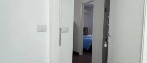 A hallway leading to a bedroom with a bed covered in a blue blanket.