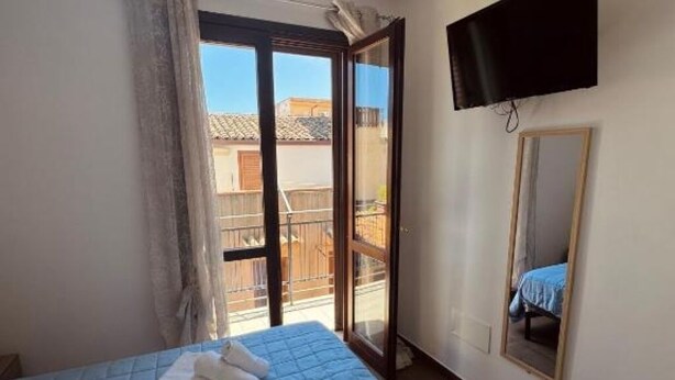A bedroom with a bed, a TV mounted on the wall, and a sliding glass door leading to an outdoor balcony. - DA REMO apartment :2 Bedroom Apartment with Balcony (Castellammare del Golfo)
