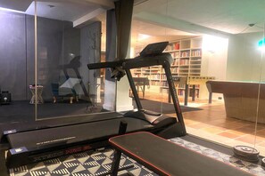 Un tapis de course dans une pièce avec un mur en verre, une bibliothèque et une table de baby-foot.