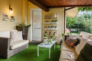 A cozy indoor space with a green artificial turf floor, two sofas, a white coffee table, and a shelving unit with potted plants.