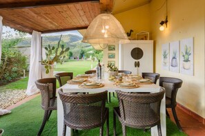 Un coin repas avec une table dressée pour six personnes, entourée de chaises en osier, sous un luminaire tressé.