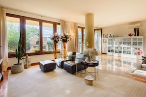 A spacious living room with a large window, a sofa set, a coffee table, and a cabinet with glass doors.