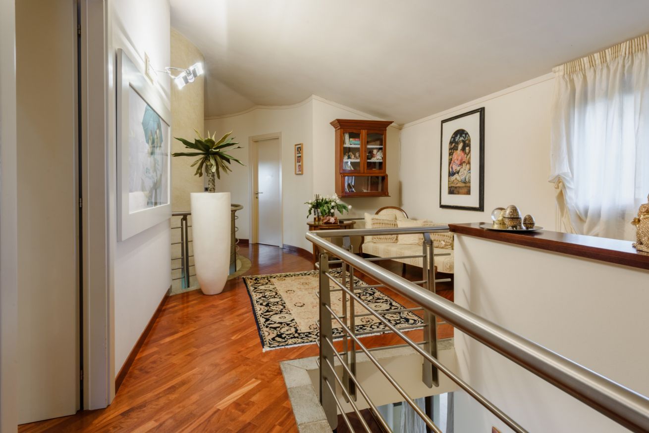 A spacious living area with a wooden floor, a staircase, a white sofa, a cabinet, and a large potted plant.