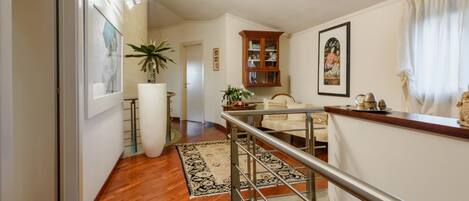 A spacious living area with a wooden floor, a staircase, a white sofa, a cabinet, and a large potted plant.