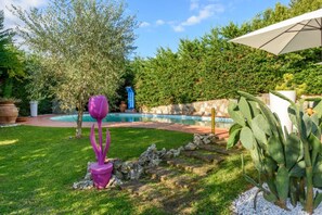 A backyard with a swimming pool, a cactus plant, and a purple sculpture.