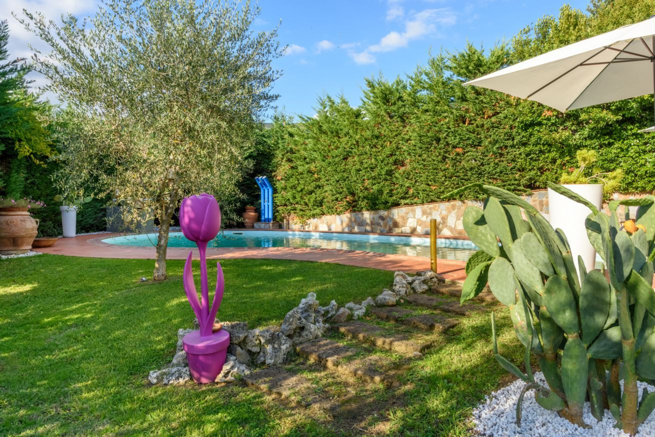 A backyard with a swimming pool, a cactus plant, and a purple sculpture.