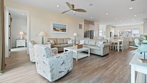 A spacious living room with a ceiling fan, a dining area, and a kitchen in the background.