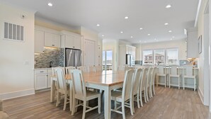 A spacious kitchen with white cabinetry, a wooden dining table, and recessed ceiling lights.