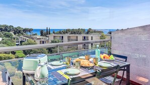 A dining table set on a balcony with a view of the sea and buildings. - Le Fidji by Interhome (La Ciotat)