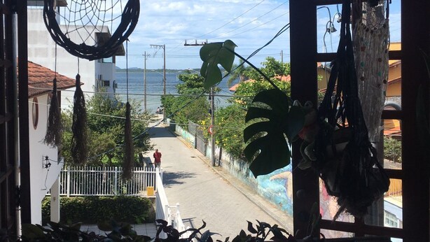 A view from a window overlooking a street with a clear sky, a body of water, and a distant building. - espiral lar (Florianopolis)