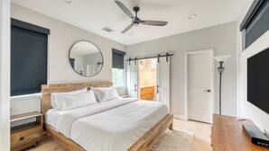 A bedroom with a wooden bed, a ceiling fan, a round mirror, and a view of a wooden deck. - Private Pool, Firepit, Patio Steps to East Austin Dining, Music, Art, Murals (Austin)