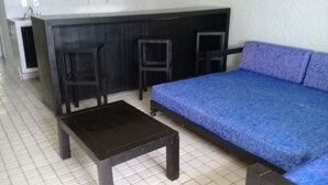 Une pièce comprenant un canapé, une petite table et deux chaises. On y trouve également un coin cuisine avec un évier et une cuisinière.
