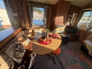 A cozy living area with a wooden sofa, a round table with a red placemat, a fireplace, and a television.