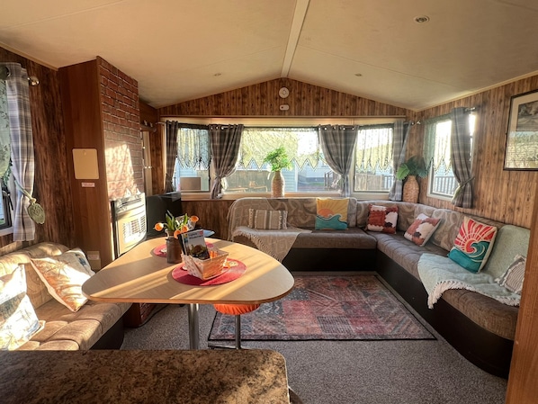 Interior acogedor de una caravana, con zona de comedor, asientos y vistas al exterior.