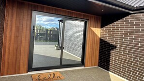 A modern building entrance with a sliding glass door, wooden paneling, and a brick wall. - Brand New 3-bedroom house with lake and mountain views, AC, lots of TVs, Te Anau (Te Anau)