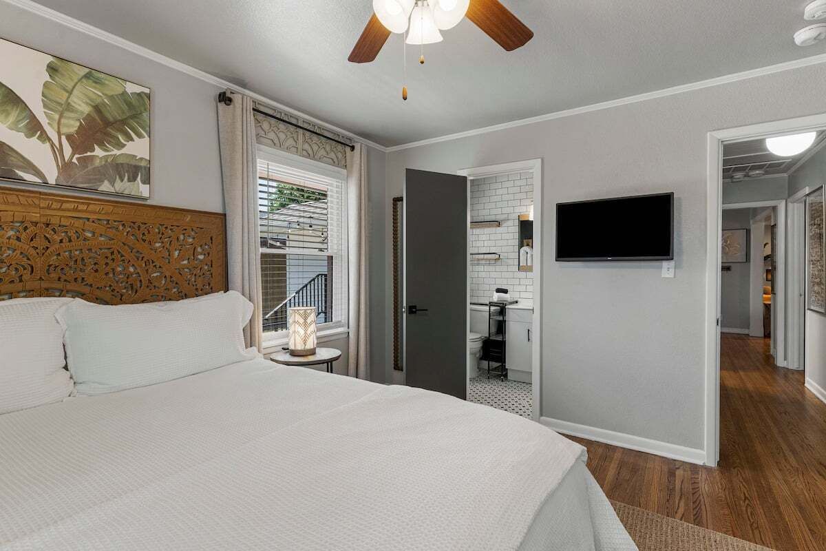Une chambre dotée d’un grand lit, d’un ventilateur de plafond, d’une télévision et offrant une vue sur la cuisine et le balcon.