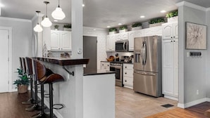 Una cocina moderna con armarios blancos, electrodomésticos de acero inoxidable y una isla central con taburetes de bar.
