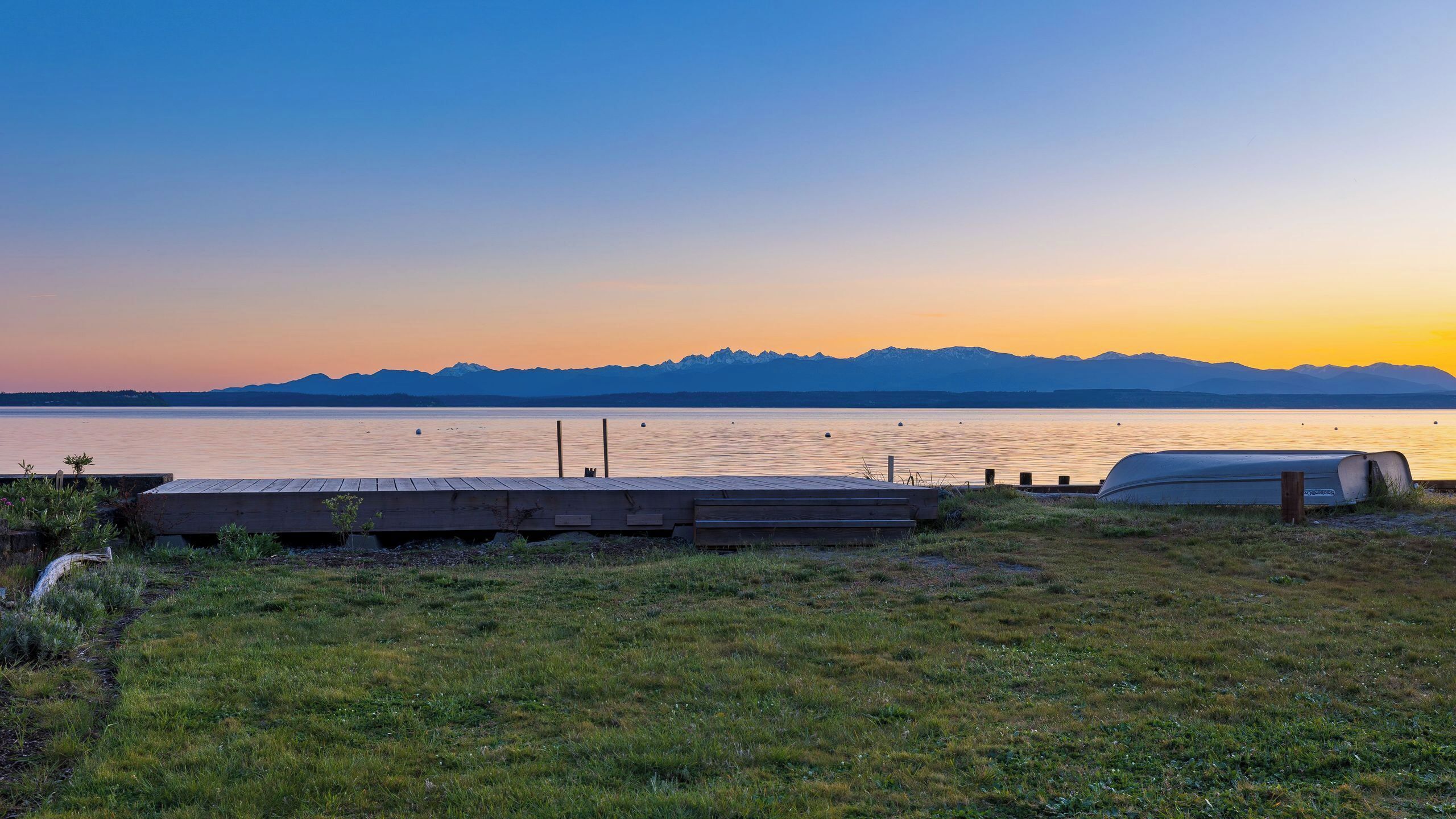 Une vue sur le lac, avec une jetée en bois, un bateau à l’abri et des montagnes en arrière-plan.