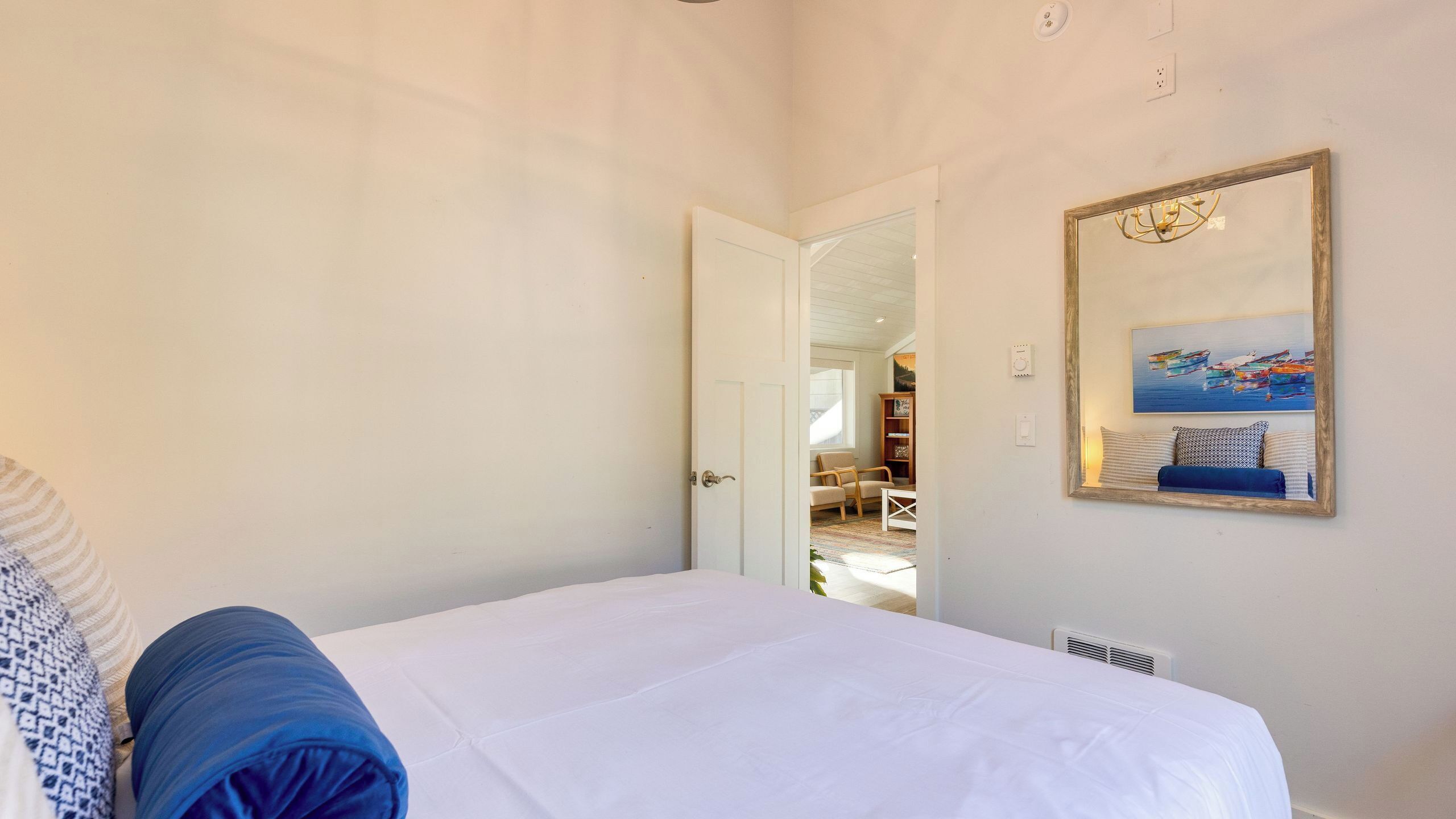 A bedroom with a bed, a door leading to a living area, and a framed picture on the wall.