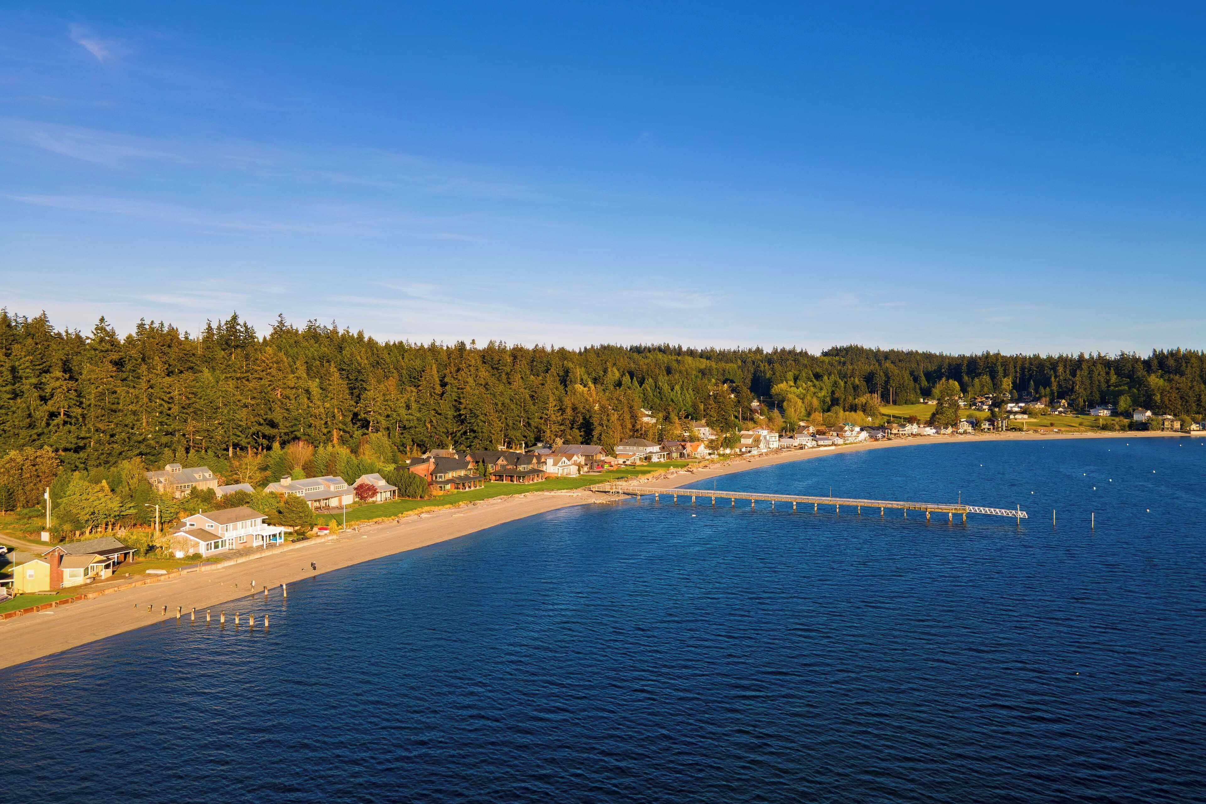 Une ville côtière dotée d’une jetée qui s’avance dans l’eau, entourée de forêts denses et d’immeubles résidentiels.