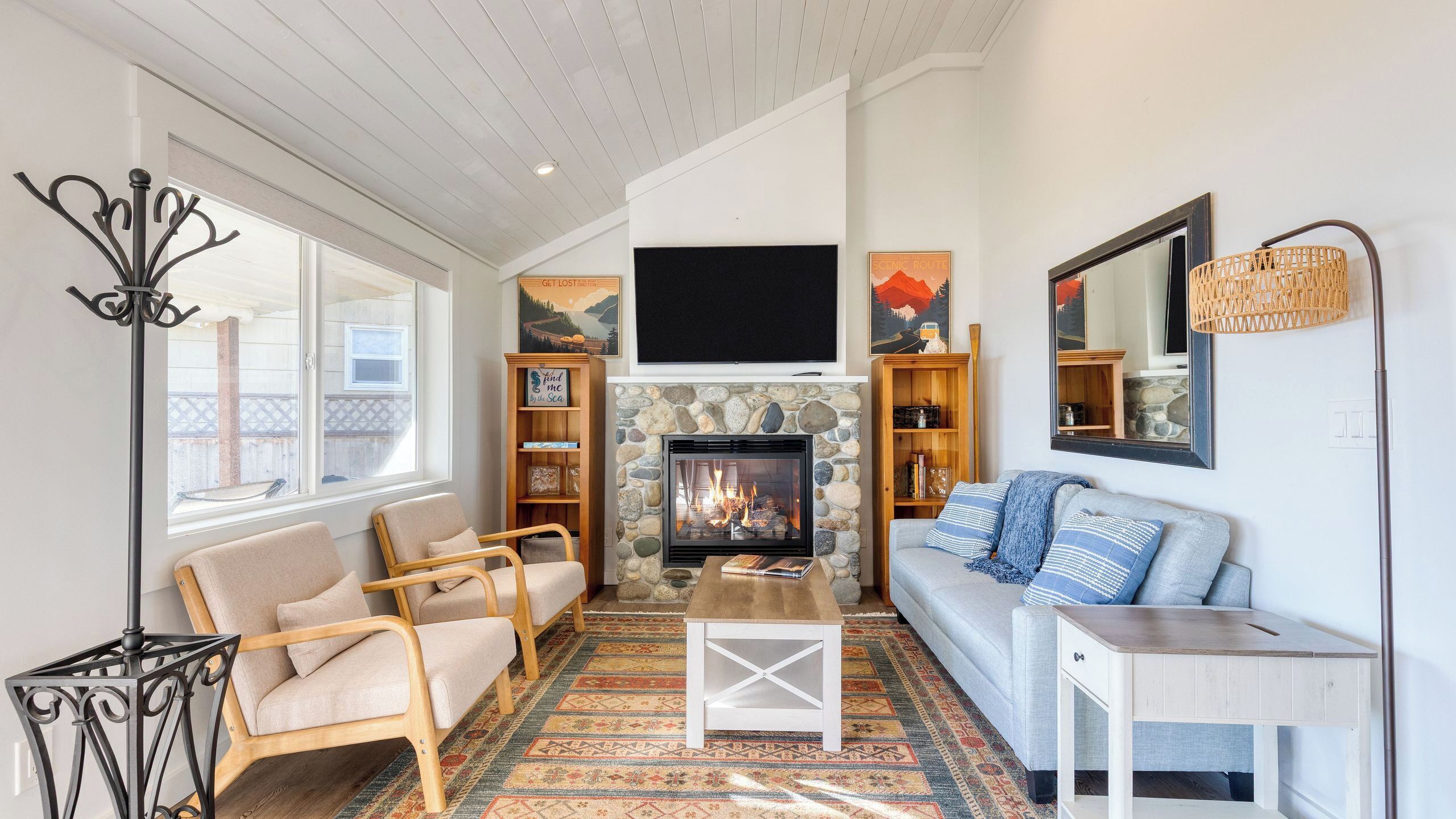 A cozy living room with a stone fireplace, a sofa, a coffee table, and a TV mounted above the fireplace.