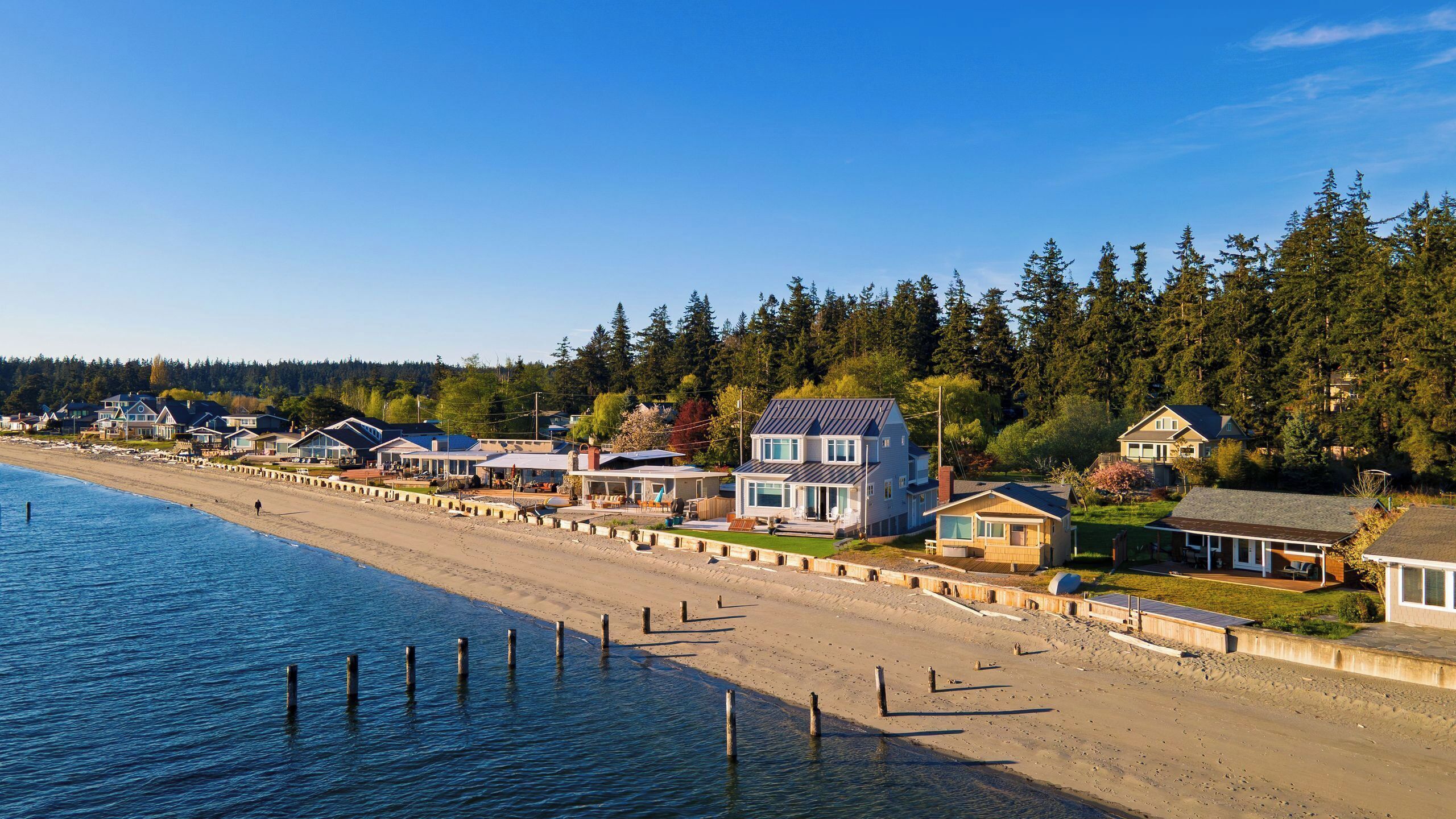 Een kustgebied met woonhuizen aan het strand, heldere lucht en een beboste heuvel.