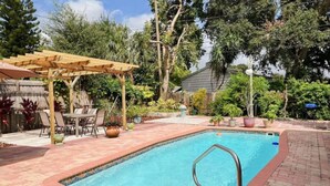 Una piscina rectangular con una pérgola de madera y un patio de ladrillo.