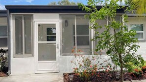 Una casa moderna con fachada blanca, puerta de cristal y un pequeño jardín con flores rojas.