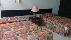 A room with two beds, each covered with colorful patterned bedding. There is a small table with a lamp between the beds. - Ideal vacation suite (Ixtapa Zihuatanejo)