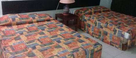 A room with two beds, each covered with colorful patterned bedding. There is a small table with a lamp between the beds.