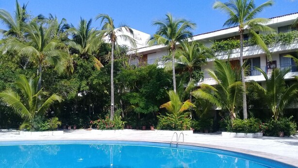 A swimming pool surrounded by palm trees and a building with balconies. - Ideal vacation suite (Ixtapa Zihuatanejo)
