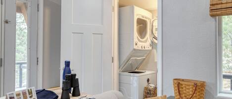 Une buanderie avec un lave-linge et un sèche-linge, une bouteille d’eau bleue, des jumelles et un sac à main en osier posés sur une table.