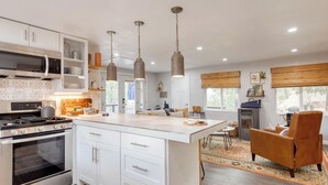 A modern kitchen with white cabinetry, a central island, pendant lighting, and a view of the outdoors.
