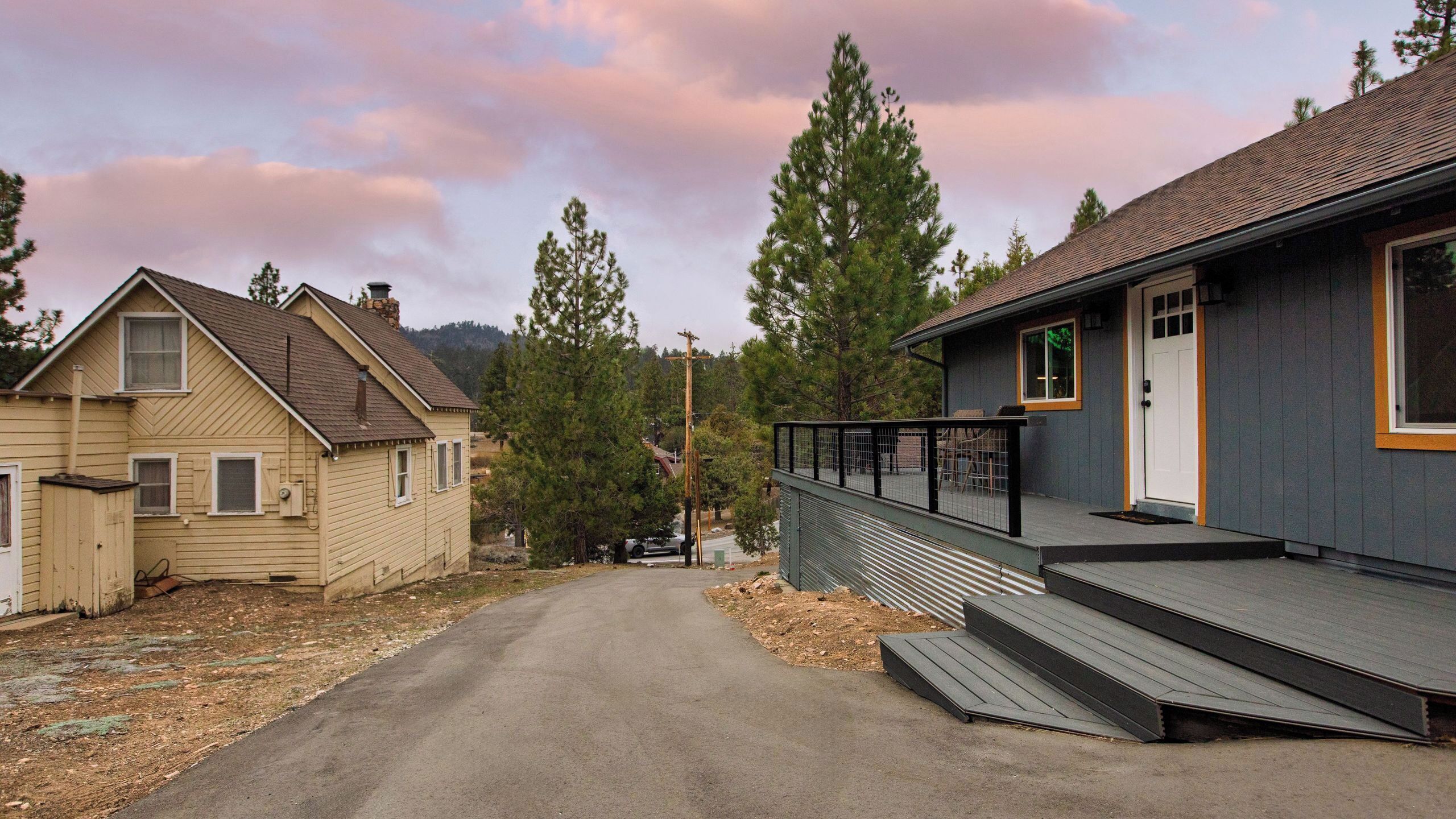 A residential street with two houses, one with a porch and steps, and the other with a garage.