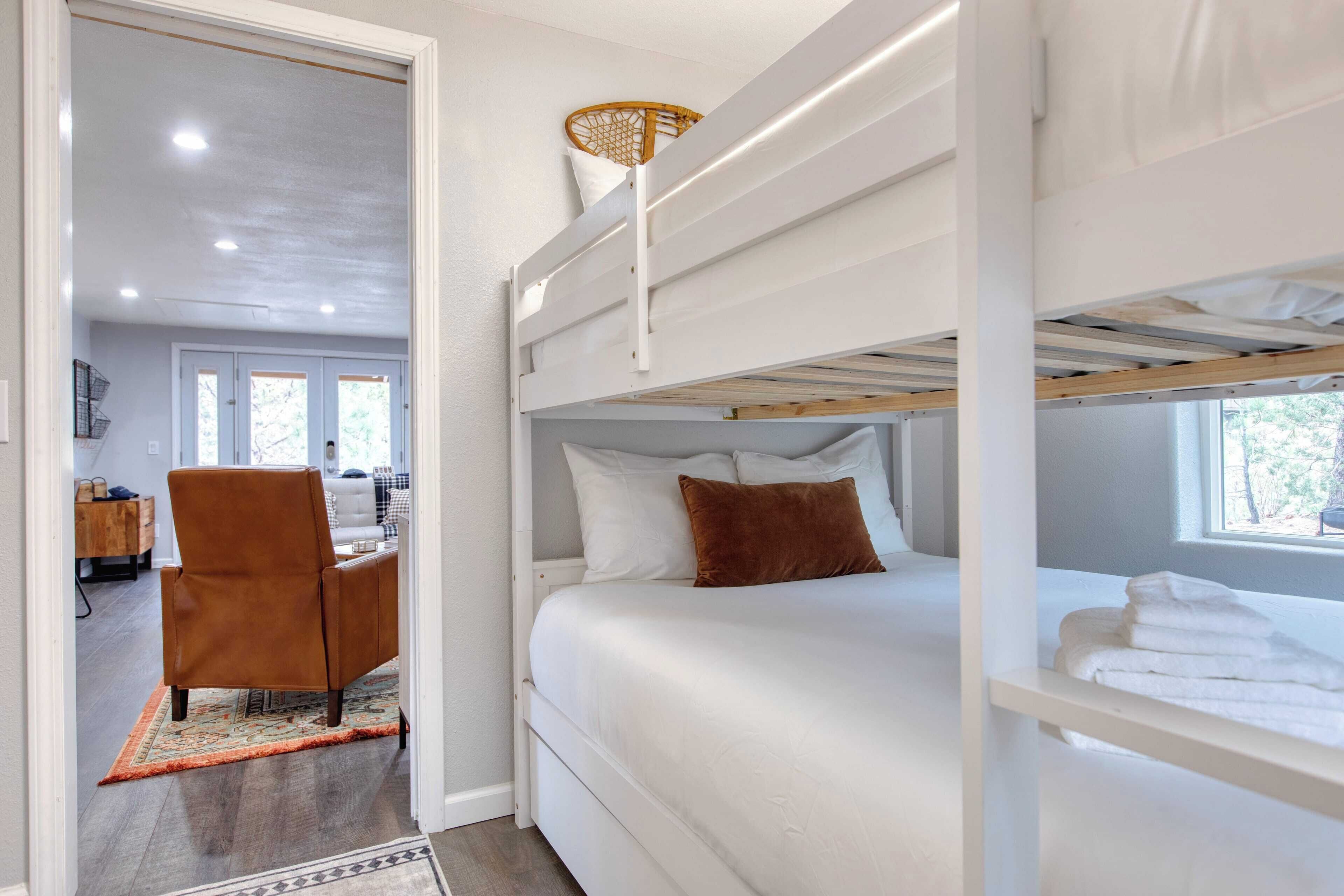 A bunk bed room with white bedding, a brown chair, and a window with daylight.