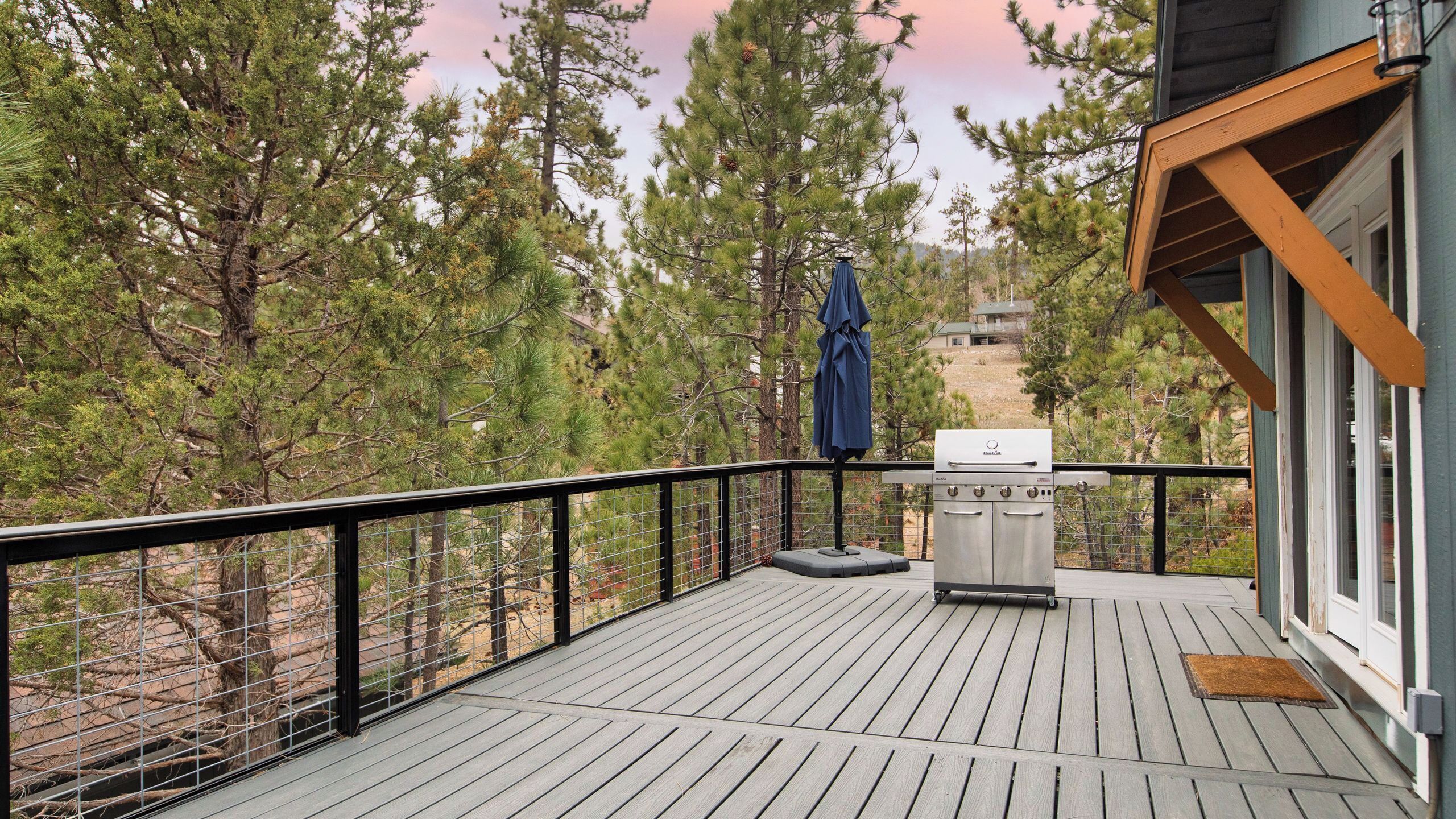Une terrasse avec un barbecue, un parasol bleu et une vue sur les arbres.