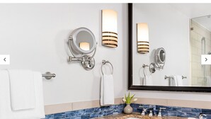 A modern bathroom with a large mirror, wall-mounted lights, a towel rack, and a sink with a decorative vase. - Marriott's Crystal Shores, Marco Island - 3 Bedroom (Marco Island)