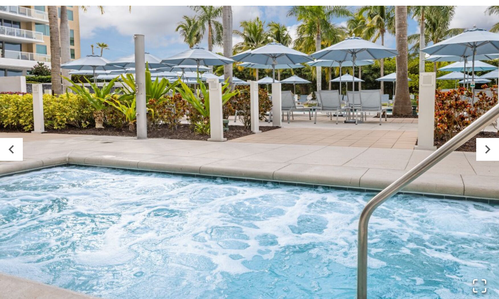 A hot tub with a view of a pool area, including lounge chairs and umbrellas.