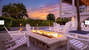 A fire pit surrounded by white Adirondack chairs, set against a backdrop of a sunset and palm trees. - Marriott's Crystal Shores, Marco Island - 3 Bedroom (Marco Island)