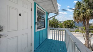 A turquoise porch with a white door marked 'A', a white railing, and a view of palm trees and a road.