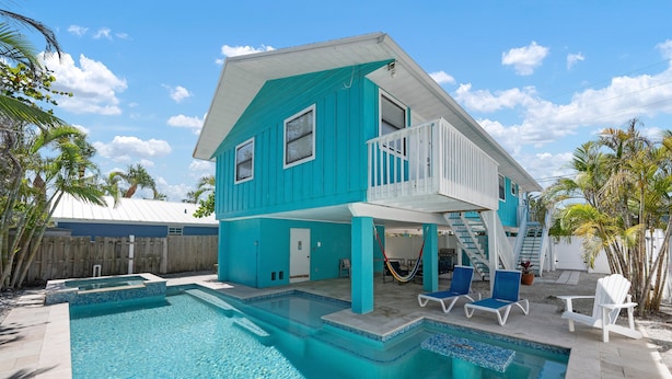 A turquoise two-story house with a swimming pool, a balcony, and a wooden fence.