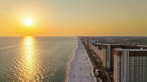 Un paysage urbain côtier avec une plage et des immeubles de grande hauteur, au coucher du soleil.