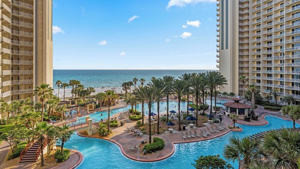 A resort with a large pool area, palm trees, and a view of the ocean. - Relax at Panama City Beach Balcony, Parking, Walk to Dining (Panama City Beach)