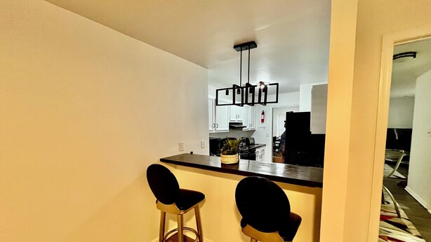 A small kitchen with a bar area, two stools, and a hanging light fixture.