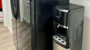 A black refrigerator with a water dispenser, white cabinets, and a wooden floor.