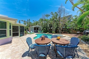 A backyard with a swimming pool, lounge chairs, and a covered seating area.