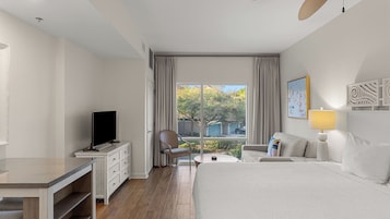 Habitación de hotel con cama, televisor en una cómoda, silla, mesita y ventana con cortinas.